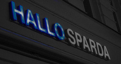 A sign with the words 'HALLO SPARDA' in large letters. The text is illuminated, with 'HALLO' in blue and 'SPARDA' in white. It appears to be part of a building facade.