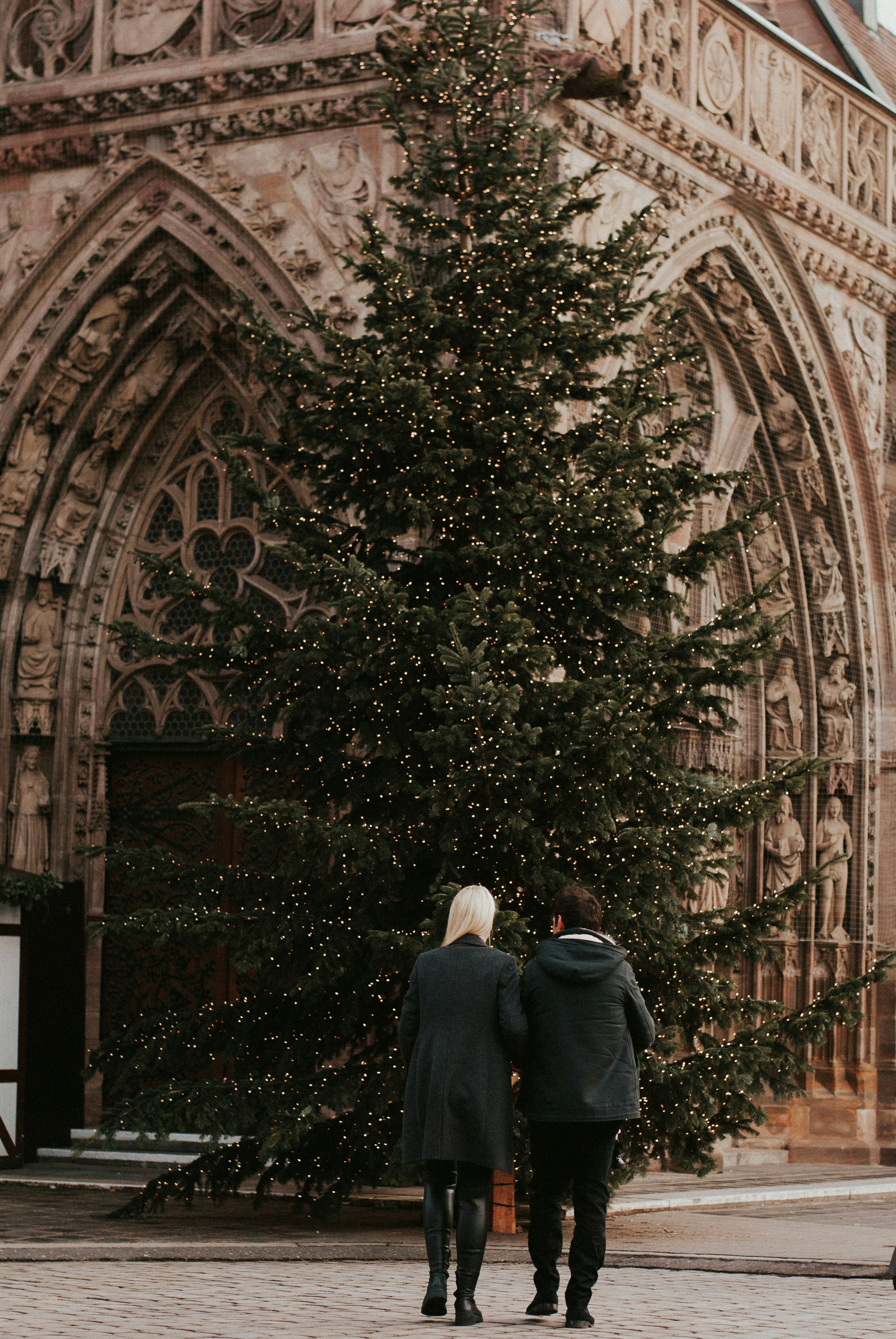 a man and woman standing next to a large tree- winter date ideas