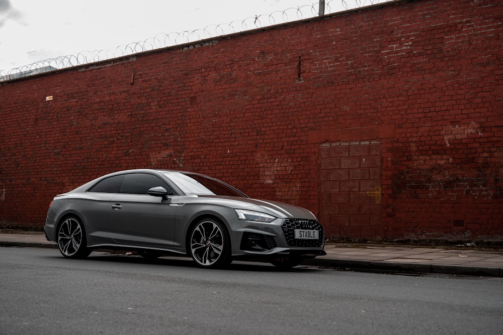 a silver car parked in front of a brick wall