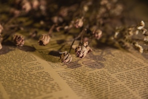 A delicate, eerie still life of wilted flowers and scattered pages from a worn book.