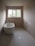 A minimalist bathroom with a freestanding bathtub positioned along one wall. The walls are unpainted, giving a raw, unfinished look. Large rectangular window at the far end brings natural light into the room. Plumbing fixtures appear bare, and an unconnected pipe is visible on the ground. The space is devoid of any decorative elements, emphasizing simplicity and functionality.
