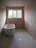 A minimalist bathroom with a freestanding bathtub positioned along one wall. The walls are unpainted, giving a raw, unfinished look. Large rectangular window at the far end brings natural light into the room. Plumbing fixtures appear bare, and an unconnected pipe is visible on the ground. The space is devoid of any decorative elements, emphasizing simplicity and functionality.