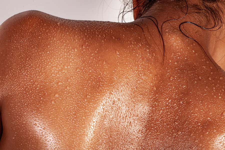 A person's back covered in beads of sweat with dark hair at the neck