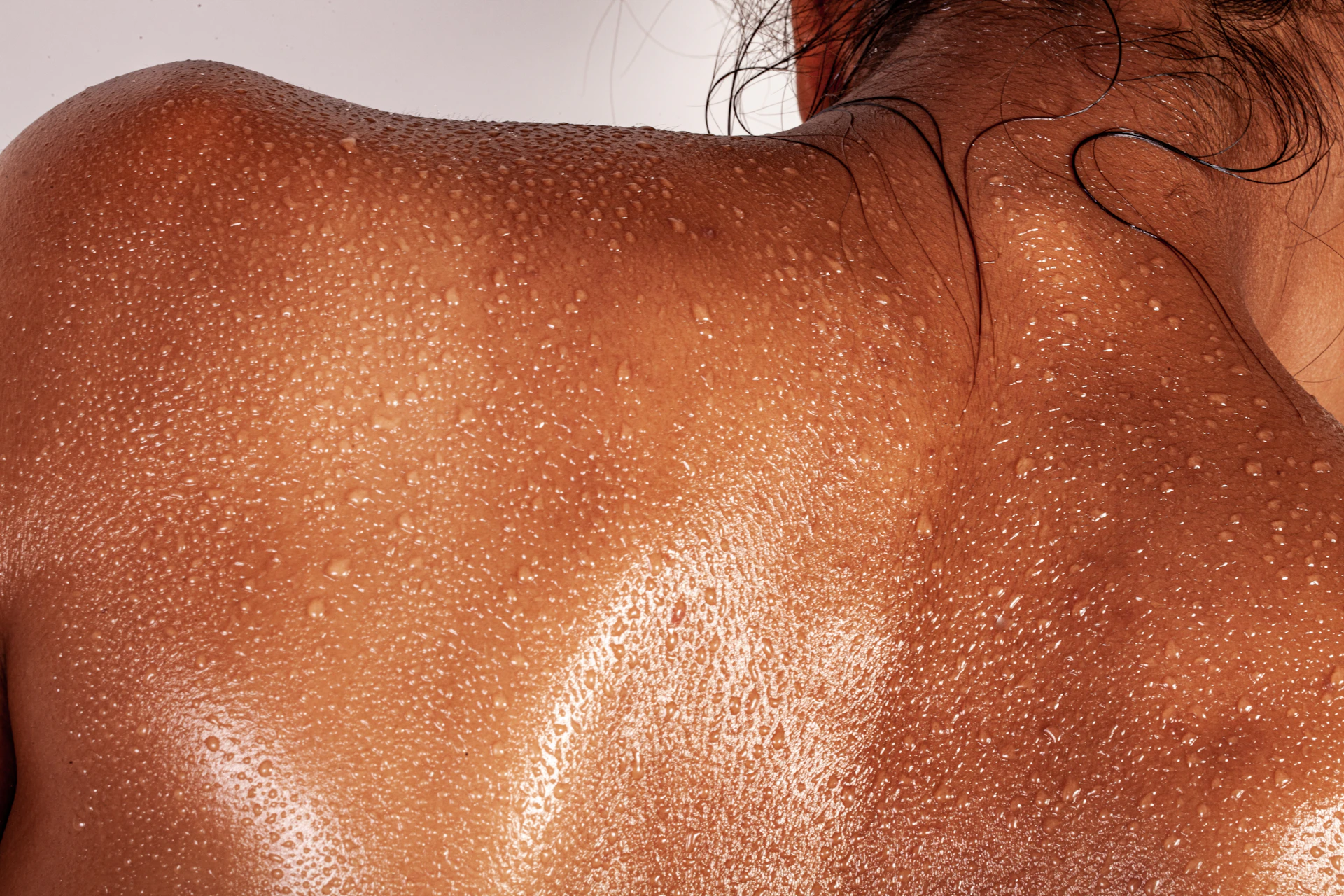 A person's back covered in beads of sweat with dark hair at the neck