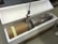 A large metal cylindrical object is partially placed inside a custom-fitted white foam case. The cylinder has a cardboard covering on one end and is lifted by a metal hook attached to a chain. It appears to be on a wooden pallet.