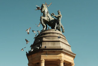 a statue of a person riding a horse with birds flying around