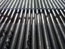 A close-up view of a series of metallic rods neatly arranged in parallel rows. The rods have a shiny, reflective surface that catches the light, and they're stamped with text near the ends.