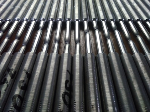A close-up view of a series of metallic rods neatly arranged in parallel rows. The rods have a shiny, reflective surface that catches the light, and they're stamped with text near the ends.