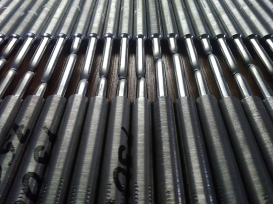 A close-up view of a series of metallic rods neatly arranged in parallel rows. The rods have a shiny, reflective surface that catches the light, and they're stamped with text near the ends.