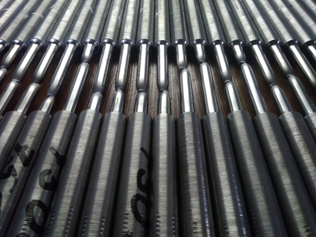 A close-up view of a series of metallic rods neatly arranged in parallel rows. The rods have a shiny, reflective surface that catches the light, and they're stamped with text near the ends.