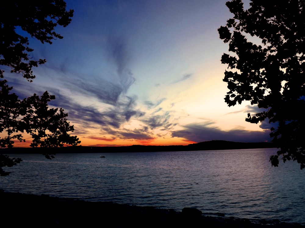 a body of water with trees and a sunset in the background