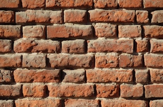 Rows of weathered red bricks form a sturdy wall. Each brick displays unique textures and variations in color, highlighting signs of aging and natural wear.