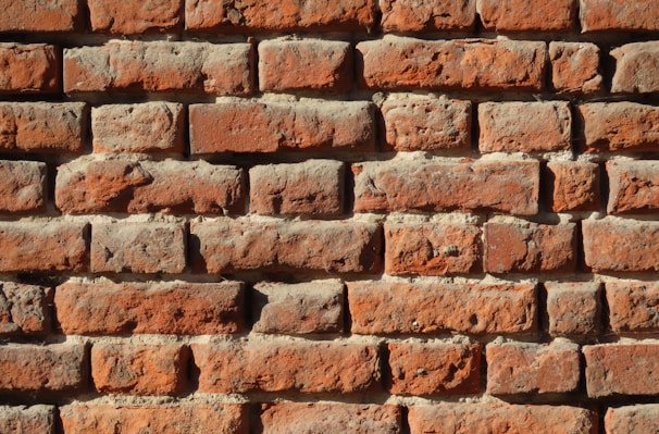 Rows of weathered red bricks form a sturdy wall. Each brick displays unique textures and variations in color, highlighting signs of aging and natural wear.