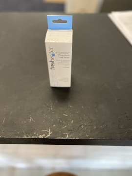 A box labeled 'FreshWater Phosphate Test Strips' with a hanging tab is placed on a dark, textured surface. The box is primarily white with blue accents and text.