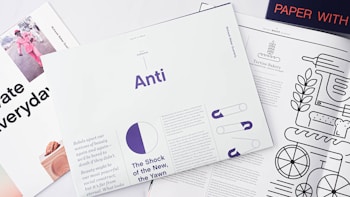 A collection of magazines and printed materials are artistically arranged on a white surface. One magazine features a monochrome design with a minimalist illustration including bread and cooking utensils. Another magazine displays bold typography with the word 'Anti' prominently in purple, accompanied by a pie chart graphic. A third piece partially visible in the top corner includes a vibrant pink image of a person dressed in a matching outfit. The layout is clean and modern, suggesting themes of design and lifestyle.