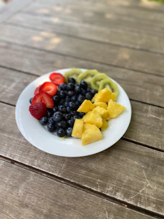 A vibrant bowl of fresh mixed fruits including strawberries, blueberries, and kiwi on a rustic wooden table.
