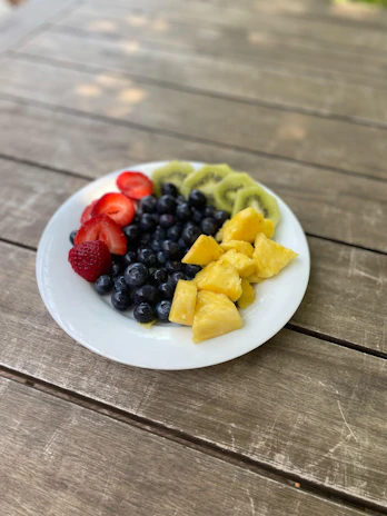 A vibrant bowl of fresh mixed fruits including strawberries, blueberries, and kiwi on a rustic wooden table.