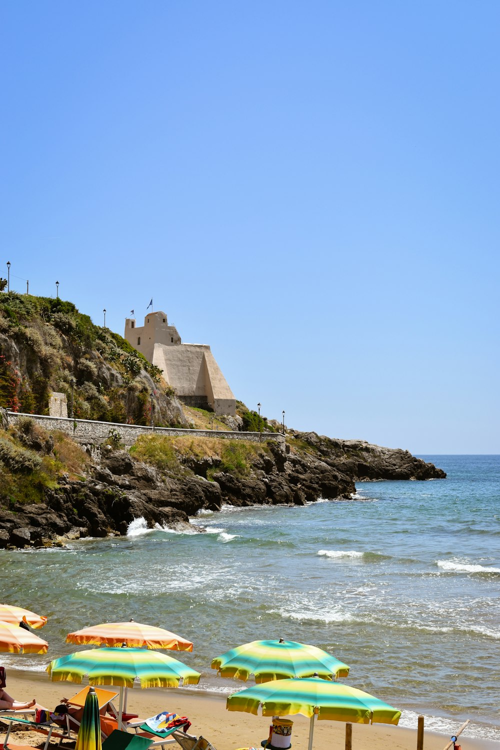 a beach with umbrellas and a castle on a hill