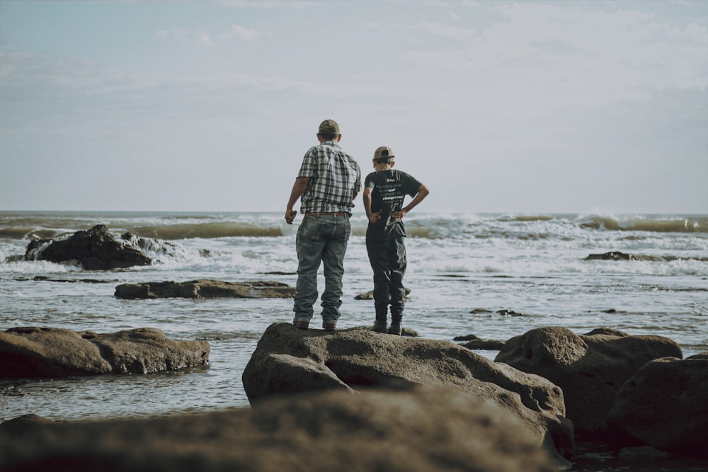 two men standing on rocks near water