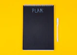 A black spiral notebook with the word PLAN written on a yellow background
