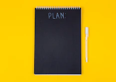A black spiral notebook with the word PLAN written on a yellow background