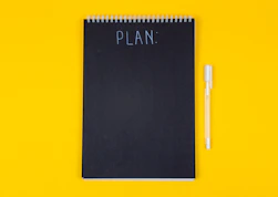 A black spiral notebook with the word PLAN written on a yellow background