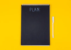 A black spiral notebook with the word PLAN written on a yellow background