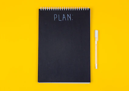 A black spiral notebook with the word PLAN written on a yellow background