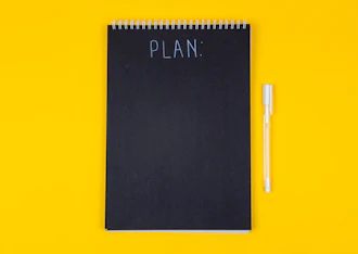 A black spiral notebook with the word PLAN written on a yellow background