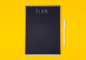 A black spiral notebook with the word PLAN written on a yellow background