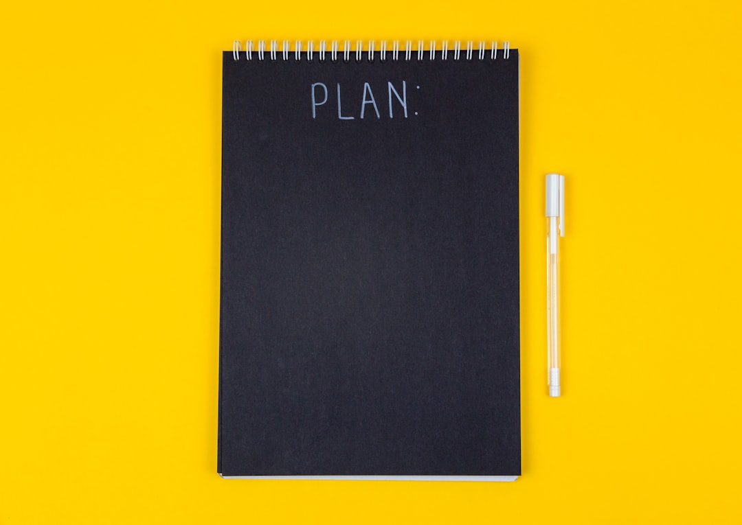 a black rectangular device, Wide view image of blank black spiral note pad and white marker with calligraphic inscriptio