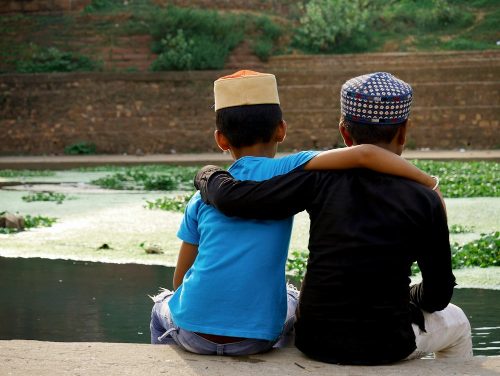 a person and a child sitting on a ledge by a body of water