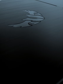 A sleek, dark metallic surface featuring an engraved logo of a stylized phoenix. The lighting is subdued, creating shadows and a moody ambiance.