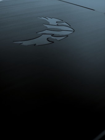 A sleek, dark metallic surface featuring an engraved logo of a stylized phoenix. The lighting is subdued, creating shadows and a moody ambiance.