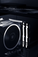 A close-up view of the interior of a computer case featuring illuminated RAM sticks with the brand name 'HyperX' visible. A large cooling fan is adjacent, showcasing the high-tech components of a gaming or performance PC setup.