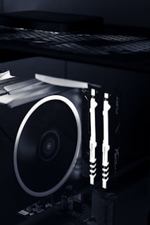 A close-up view of the interior of a computer case featuring illuminated RAM sticks with the brand name 'HyperX' visible. A large cooling fan is adjacent, showcasing the high-tech components of a gaming or performance PC setup.