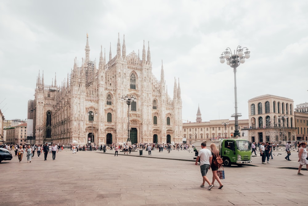 un grande edificio in pietra con molte finestre e persone che passeggiano con il Duomo di Milano sullo sfondo