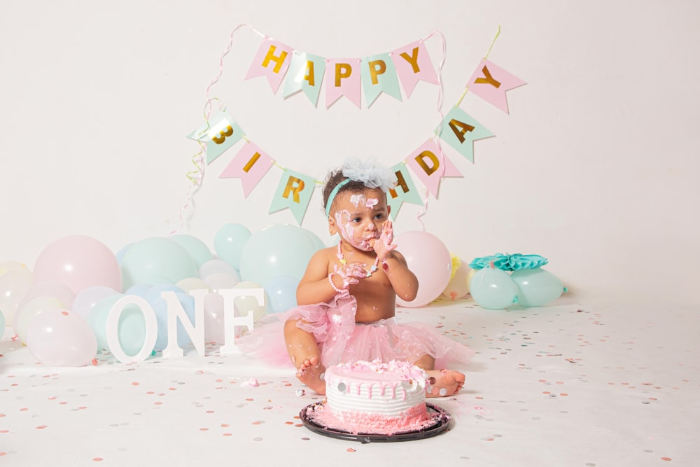 a baby sitting in front of a birthday cake with a birthday hat on