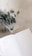 An open planner is displayed on a light marble surface, with a sprig of eucalyptus leaves placed on the table next to it. The planner shows sections for weekly and daily planning.