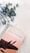 A stylish planner labeled 'Goal Planner' rests on a marble surface. The planner has an elegant design with a pastel pink and peach cover featuring minimalistic black leaf illustrations. Adjacent to the planner is a sprig of dried eucalyptus, adding a natural, calming touch to the scene.