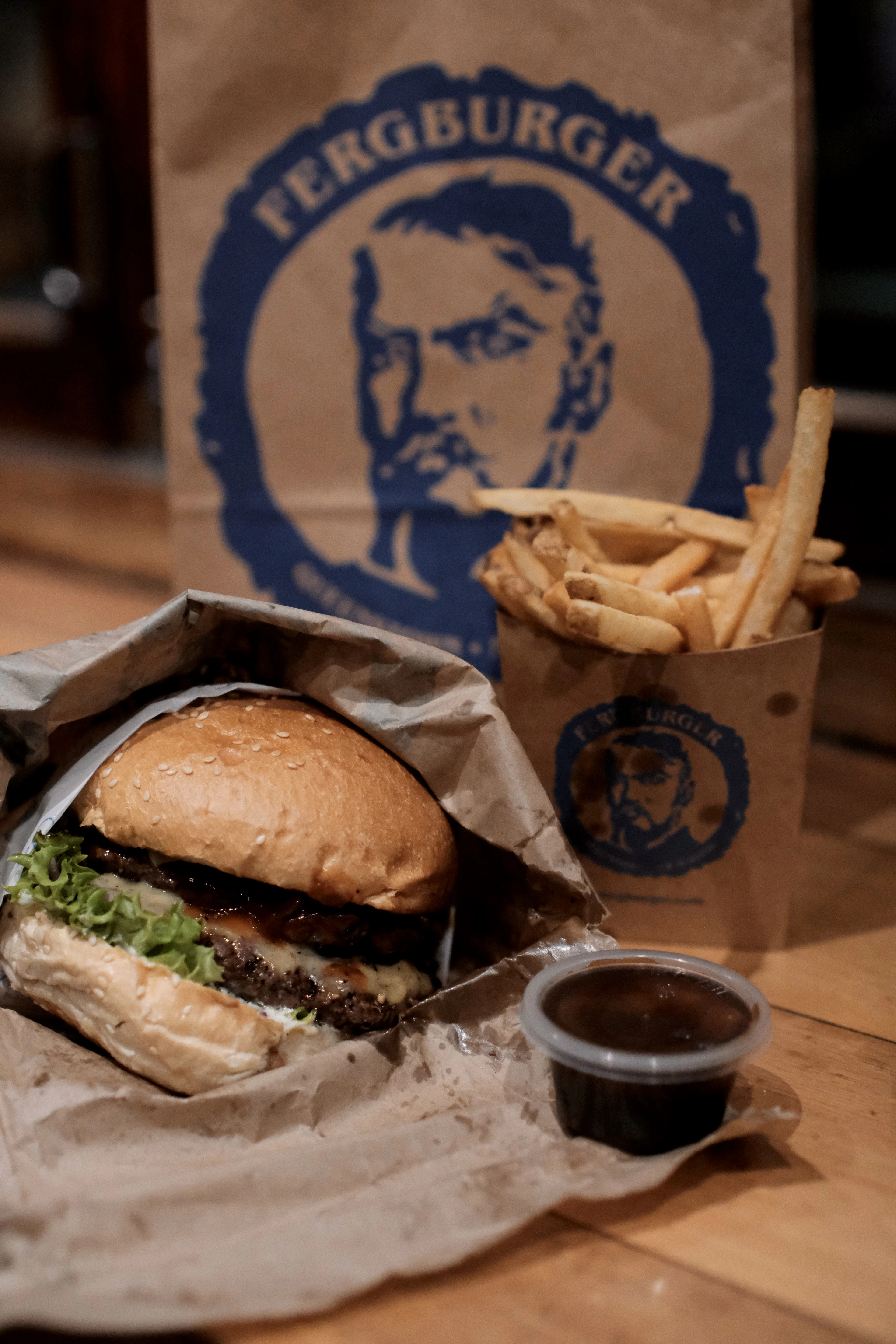 A Fergburger burger unwrapped on its paper next to a carton of fries and the shop's branded bag, in Queenstown, New Zealand.