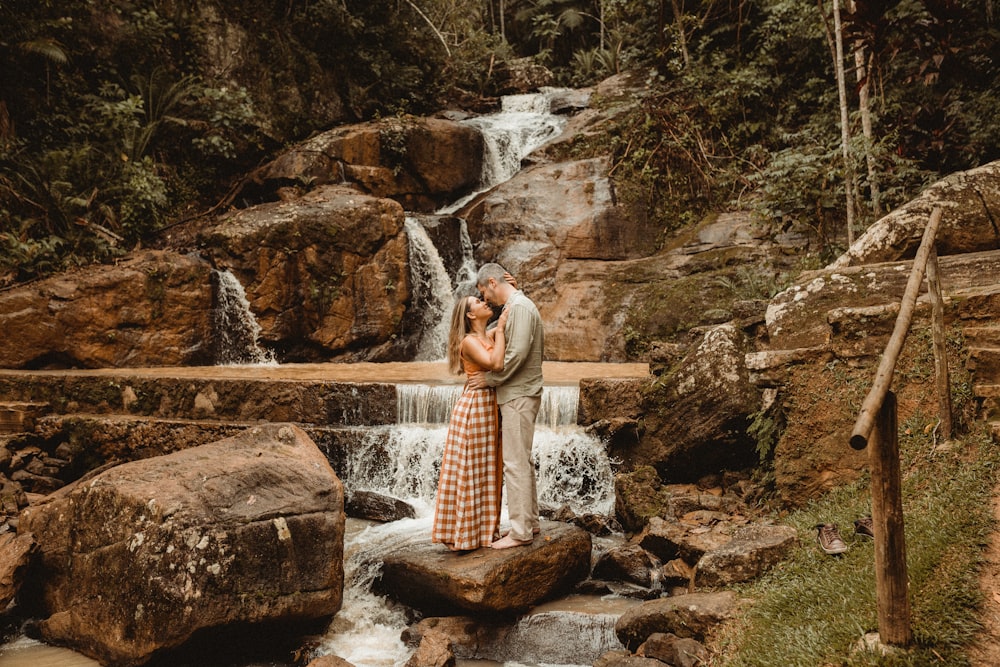 a man and woman kissing in front of a waterfall