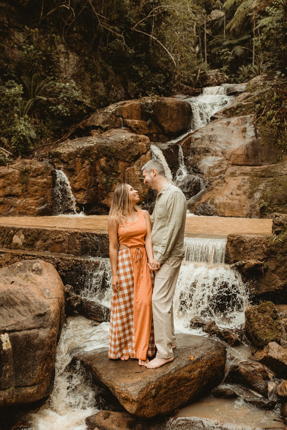 a man and woman kissing in front of a waterfall