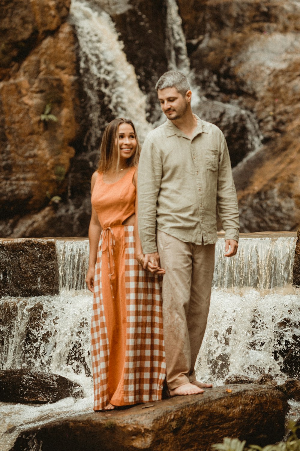 a man and woman standing in front of a waterfall