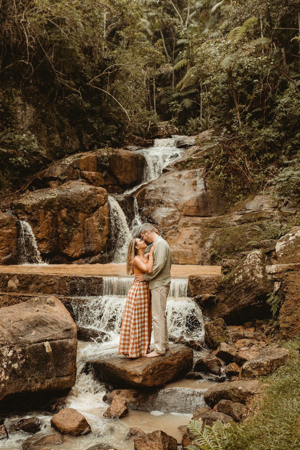 a man and woman kissing in front of a waterfall