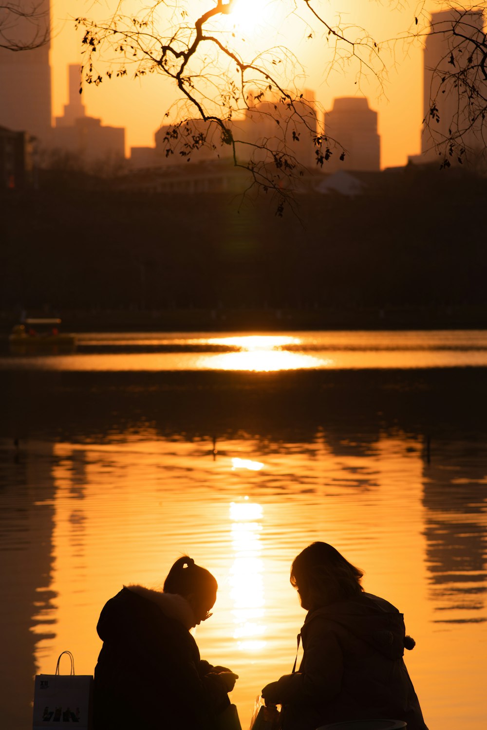 people sitting on a bench looking at the water at sunset