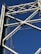A close-up view of a steel bridge's structural framework against a clear blue sky. The intricate lattice of beams forms a geometric pattern, highlighting the engineering and design of the bridge.
