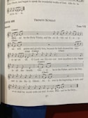 A page from a music book featuring a religious hymn titled 'Trinity Sunday' with sheet music and lyrics. The page number is 87, and the hymn is set in Tone VII. There are notations for cantor and choir parts, with musical notes and lyrics including religious themes.