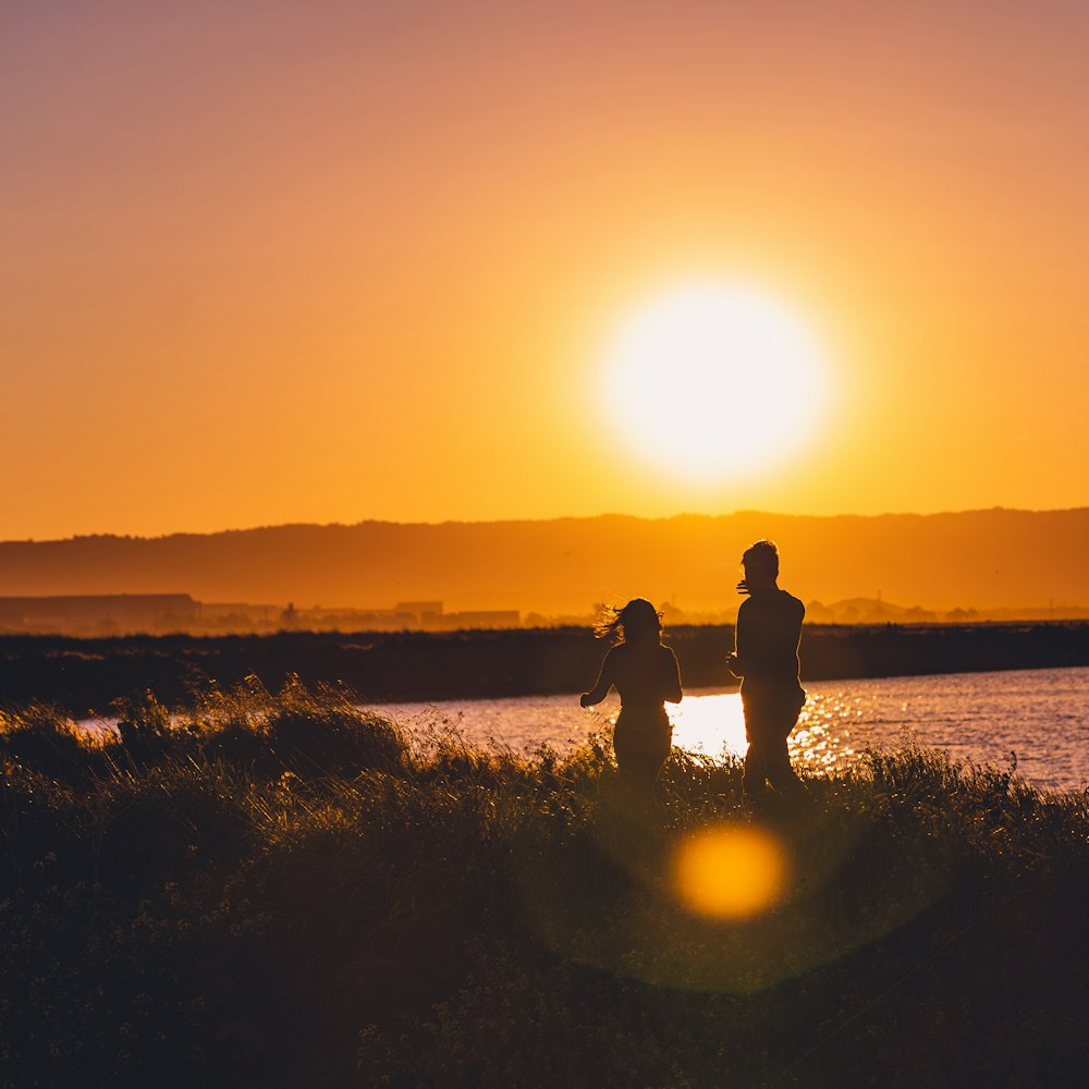 a couple of people standing on a beach with the sun setting