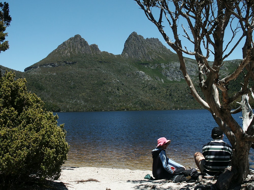 a couple of people sitting on a beach looking at a body of water